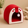 Red arched Cat Cave Bed with hanging pom-pom ball toy at entrance